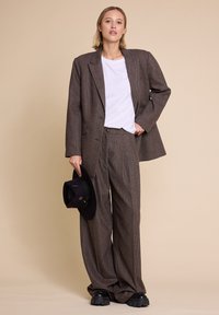 Brun rutete dress med en oversized blazer og vide bukser. Båret over en hvit t-skjorte, holder en mørk hatt. Svart platå sko.