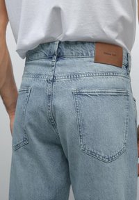 Light blue denim jeans with a high waist, featuring a brown leather patch. Classic five-pocket design and slightly faded texture.