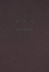 Tmavofialová tkanina s pruhovanou textúrou a razeným brandingom "CPH STUDIOS" v čiernej farbe. Minimalistický a súčasný dizajn.