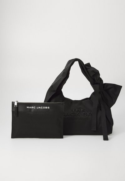 Grand sac fourre-tout en nylon noir avec des poignées nouées, comportant un texte en relief. Inclut une pochette zippée assortie avec le texte "MARC JACOBS".