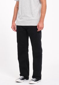 Sorte denim-bukser med lige ben-design, kombineret med sorte sneakers. Materialet er robust med en klassisk pasform, velegnet til afslappet brug.