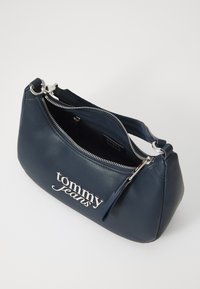 Navy leather handbag with a rounded shape, silver hardware, and a zip closure. Features "tommy jeans" logo in silver on the front.