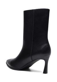 Elegantiška juoda odinė batelė iki blauzdos su smailia nosimi ir plonu aukštu kulnu, vaizduojama iš šono ant balto fono.