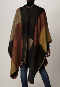 Wool blend poncho in geometric patterns, featuring shades of black, brown, gold, and gray, with fringe detailing along the edges.