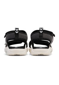 Sorte mesh sandaler har dobbel justerbare remme, en polstret sål og en struktureret hvid sål. En sort træksløjfe med en hvid pilaccent er inkluderet.