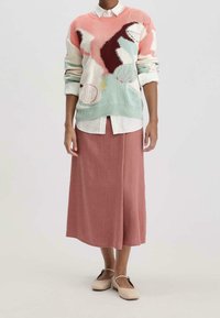 Pull en tricot multicolore avec motifs abstraits, associé à une jupe en lin rose pastel et des chaussures beige sans lacets.