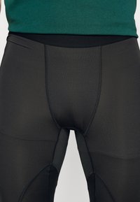 Svarta träningsleggings med en slät yta, som har en bred elastisk midjeresår och förstärkta sömmar längs kanterna.