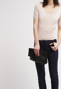 Musta nahkainen clutch-laukku, jossa on taitettu muotoilu, yhdistettynä sopivan istuvaan beigeen paitaan ja kapeneviin tummansinisiin housuihin. Sileä pinta ja tyylikäs siluetti.