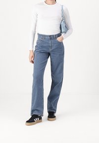 Blue striped corduroy pants with a high waist, paired with a white long-sleeve top and black sneakers with white stripes. Small blue handbag.