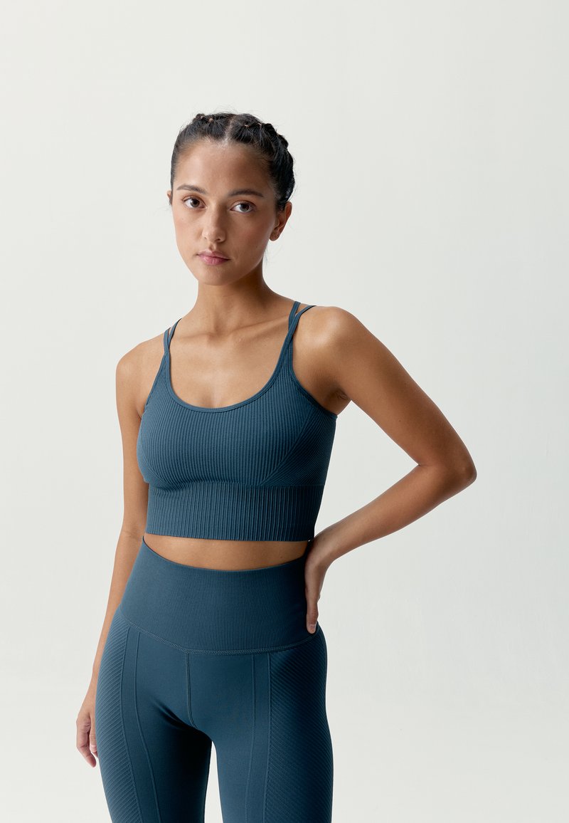 Mörk teal ribbad sport-bh med smala band och en kort design, kombinerad med matchande högmidjade leggings med vertikala sömmar.