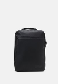Mochila de cuero negro con una textura suave, forma rectangular, un bolsillo frontal con cremallera y un parche de logo en la parte inferior.