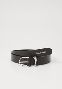 Juodas odinis diržas su sidabriniu metaliniu užsegimu, pasižymintis švelniu dizainu ir logotipo žymė su "Calvin Klein" balta spalva.