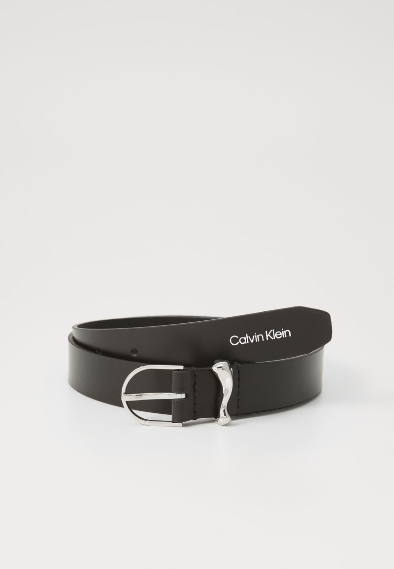 Sort læderbælte med en sølvfarvet metalspænde, der har et strømlinet design og et logomærke med "Calvin Klein" i hvid tekst.
