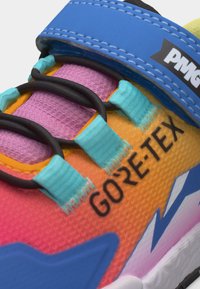 Κοντινό πλάνο πολύχρωμου αθλητικού παπουτσιού που δείχνει μπλε λουράκι, μαύρα ελαστικά κορδόνια και πορτοκαλί-ροζ δίχτυ με ετικέτα "GORE-TEX" στο πλάι.
