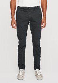 Black cotton trousers with a slim fit, featuring a button closure, belt loops, and side pockets. Paired with light gray sneakers.