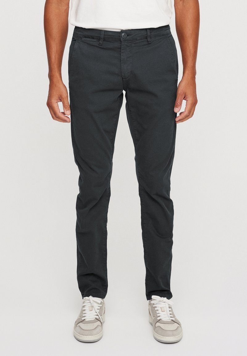 Black cotton trousers with a slim fit, featuring a button closure, belt loops, and side pockets. Paired with light gray sneakers.