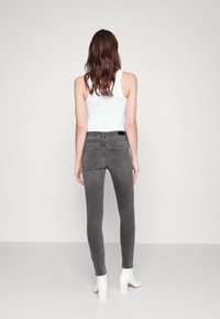 Jeans gris ajustados con bolsillos traseros, costuras acentuadas y una cinturilla negra; combinados con una camiseta sin mangas blanca y botas tobilleras blancas.