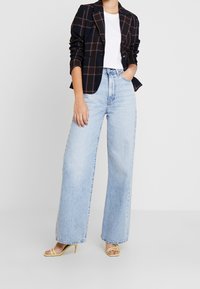 Czarna kraciasta marynarka na białym t-shircie, zestawiona z jasnoniebieskimi szerokimi spodniami i żółtymi sandałami na obcasie. Gładka tkanina i luźny krój.