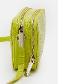 Borsa a mano di color verde lime con effetto coccodrillo, zip in tono oro, manico singolo e forma rettangolare. Superficie testurizzata, design compatto.