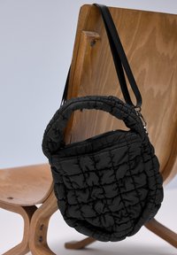 Sac à main rond noir matelassé avec poignée courte et longue bandoulière suspendu au dossier d'une chaise en bois.
