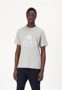 Tricou din bumbac gri, cu mâneci scurte și decolteu rotund; prezintă text alb imprimat "EST. 2011 ES DEUX Sporting Goods" pe față.