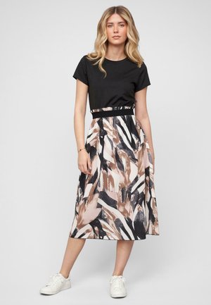 Un haut noir à manches courtes associé à une jupe midi à motifs en beige, noir et blanc avec des designs abstraits, mettant en valeur une taille cintrée.