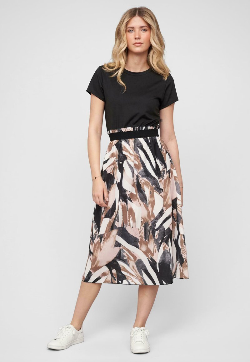 Un haut noir à manches courtes associé à une jupe midi à motifs en beige, noir et blanc avec des designs abstraits, mettant en valeur une taille cintrée.