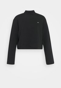 Svart kort tröja med hög krage, långa ärmar och en liten logodetalj på bröstet. Tillverkad av mjukt, strukturerat tyg.