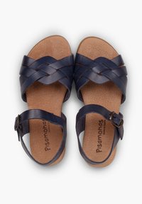 Navy blue nahka sandaalit, joissa on kudottu remmin muotoilu, taustalla nilkkaremmi soljella ja korkkinen pohja mukavuutta varten.