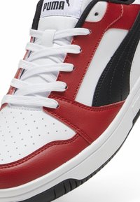 PUMA tenisice s gornjim dijelom od bijele kože i crvenim te crnim naglascima. Perforirani detalji na prstima, ravne bijele vezice i crna gumena potplat.