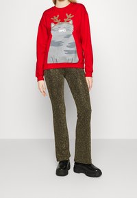 Sudadera roja con gráfico de un gato gris con astas, combinada con pantalones acampanados de punto dorado brillante y zapatos de plataforma negros.