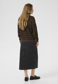 Braun gestreifter Pullover mit geripptem Textur, kombiniert mit einem langen schwarzen Jeansrock. Das Modell trägt schwarze Slippers. Einfaches, lässiges Outfit.