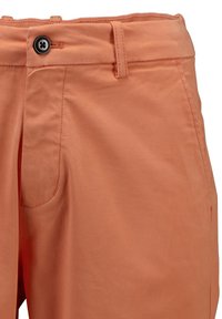 Un pantalon couleur pêche présente une fermeture éclair et un bouton, des passants de ceinture, une poche latérale et une texture lisse et douce.