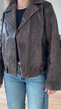 Veste de moto en faux cuir brun avec une fermeture éclair à l'avant, un col cranté et des poches latérales. Présente un design court et une finition texturée.