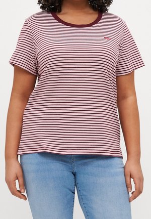 Kvinde iført en kortærmet t-shirt med lyserøde og mørkerøde striber, mørkerød krave og lyseblå jeans.