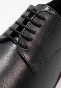 Chaussure habillée en cuir noir avec laçage fermé, coutures détaillées et surface lisse et polie, présentée en gros plan.