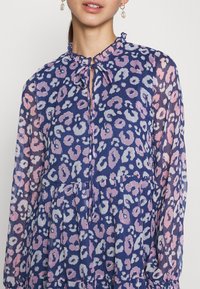 Blus med blommönster i nyanser av blått och rosa, med volangkrage och knytning. Lättviktigt tyg med långa ärmar.