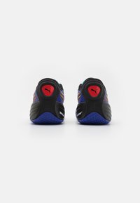 Zwarte en paarse sportschoenen met een getextureerde zool, voorzien van een rode accenten bij de hiel en gele strepen op de bovenkant.