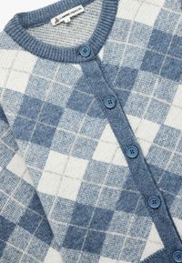 Niebieski i biały cardigan w wzory z motywem w kratkę, dzianinowa struktura, okrągły dekolt oraz niebieskie guziki z przodu.