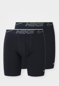 Deux paires de boxers Nike noirs avec une large ceinture affichant le nom de la marque en blanc et une ligne d'accent vert en haut.
