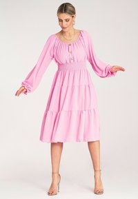 Różowa sukienka w warstwach z długimi, bufiastymi rękawami i marszczoną talią. Posiada guziki z przodu oraz zwiewny, lekki materiał.