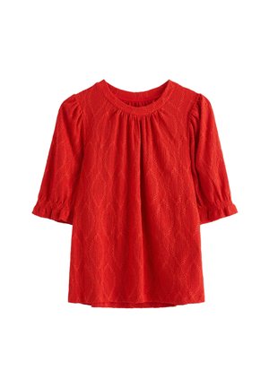 Punainen kuvioitu pusero, jossa on timantinmuotoinen silmukkakuvio, pyöreä pääntie ja kolmen neljänneksen mittaiset liehukehihat, joissa kootut hihansuut.