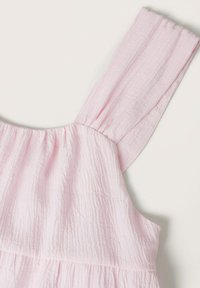 Robe sans manches en tissu texturé rose clair avec larges bretelles et encolure froncée sur un fond uni.
