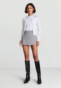 White ribbed long-sleeve top with cut-out shoulders, paired with a light gray mini skirt and knee-high black heeled boots.
