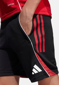 Zwarte sportieve shorts met rode zijstrepen, witte piping en het Adidas-logo. Gemaakt van lichtgewicht, ademende stof.