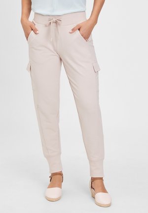 Femme portant un pantalon jogger cargo beige clair avec taille à cordon et poches avant, associé à des espadrilles compensées blanches.