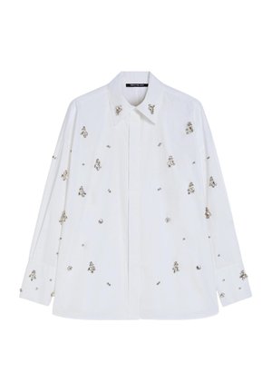 Camicia bianca in cotone con colletto, decorata con ornamenti argentati e piccoli motivi floreali su tutta la superficie. Maniche lunghe con polsini a bottoni.