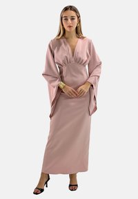 Vestido largo de satén rosa con un pronunciado escote en V, cintura fruncida y mangas anchas; combinado con sandalias de tacón negro. Textura suave, diseño formal.