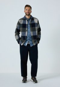 Checked wool jacket in shades of gray and navy, layered over a denim shirt. Paired with dark pants and multicolored sneakers.