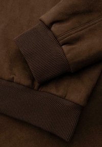 Ruskea fleece-sweatshirt, jossa on ribbireunat hihansuissa ja helmassa, pehmeä tekstuuri ja tasainen väri. Yksityiskohtainen ompelu saumoissa.
